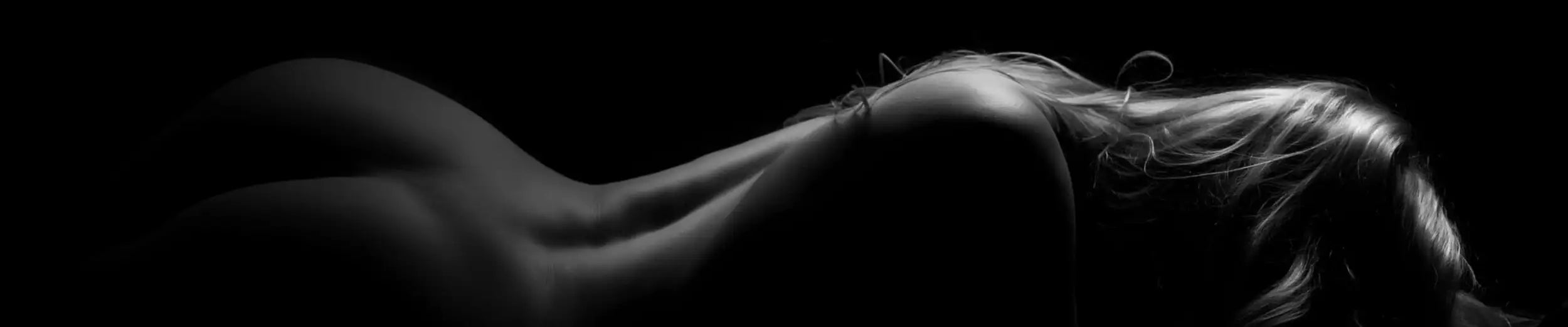 A black-and-white photograph of a nude woman lying on her side with long, flowing hair.