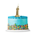 A glittery gold novelty candle shaped like a penis with a lit flame on a blue frosted cake from lady jane adult shop