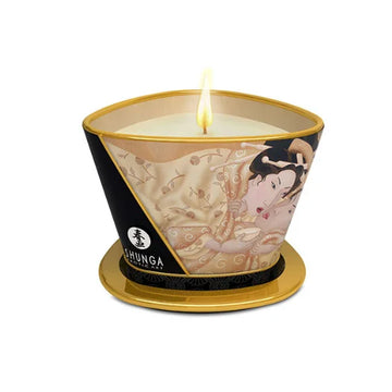 A lit creamy white shunga vanilla massage candle in a gold-rimmed ceramic vessel with an elegant women illustration