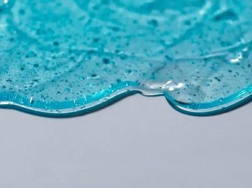 A translucent blue gel with a glossy, viscous texture and scattered dark specks.