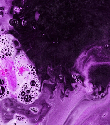 A vibrant purple and black bath bomb with swirling patterns, bubbles, and a glossy surface.